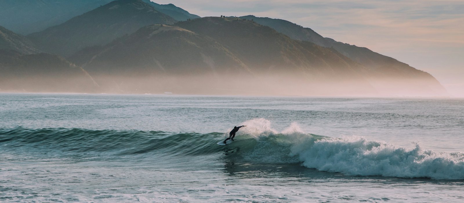 Surfer auf einer Welle vor einer Bergkette
